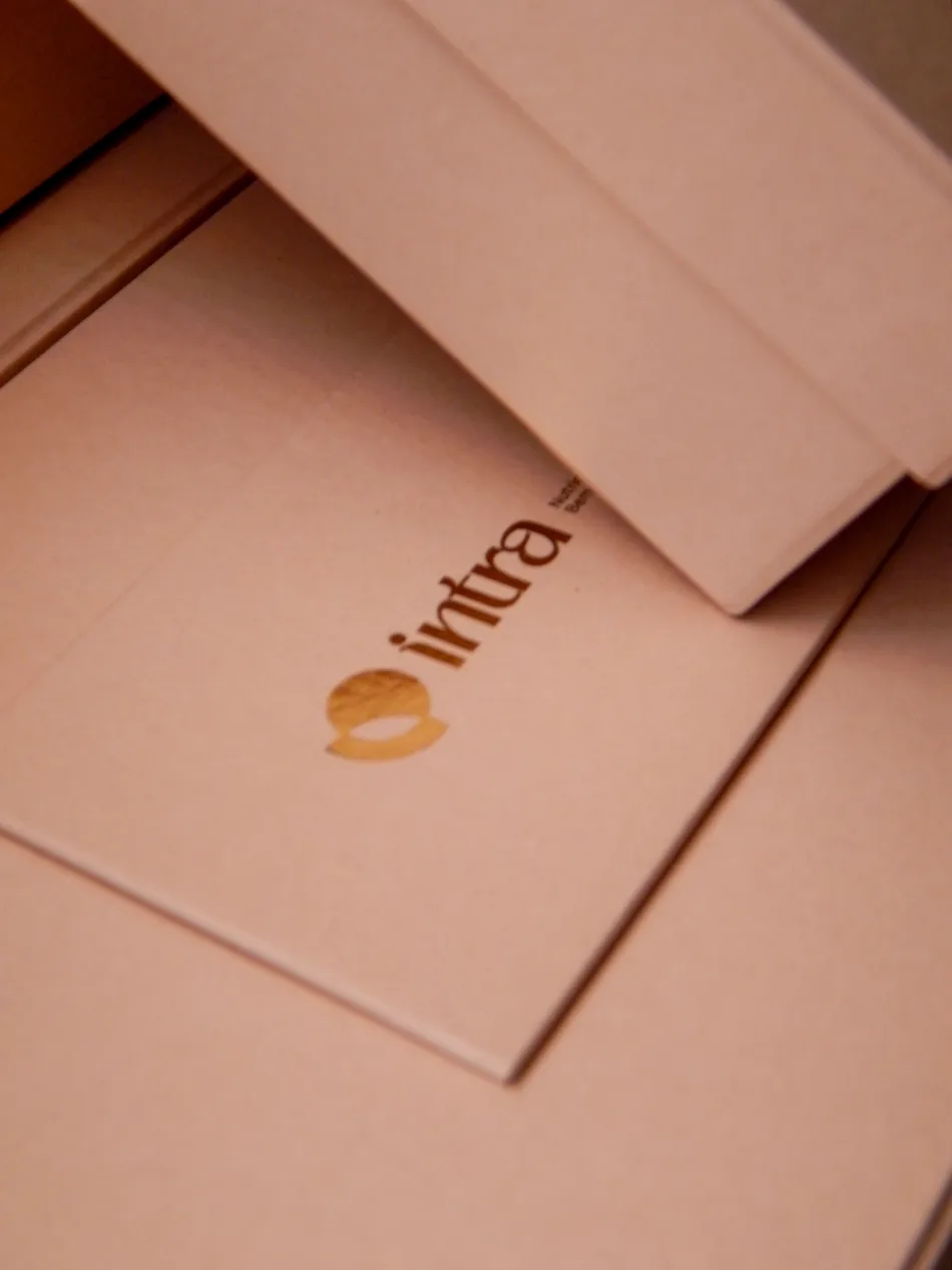 Caixa rosé fechada, com a marca Intra em hot stamping dourado sobre a tampa