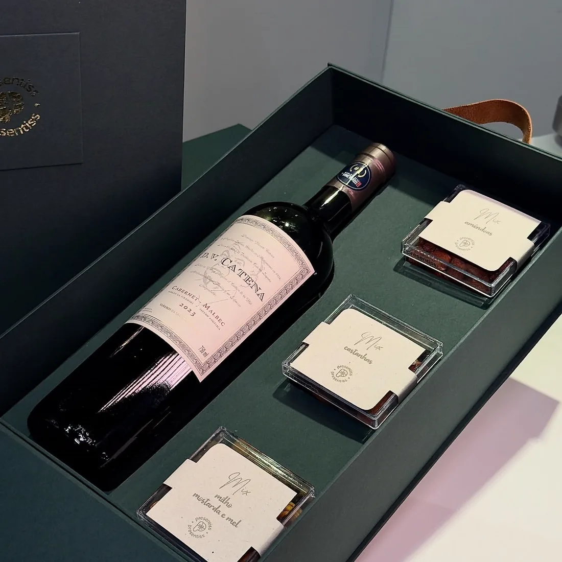Caixa verde aberta com uma garrafa de vinho no encaixe recortado e três potes de mix de castanhas